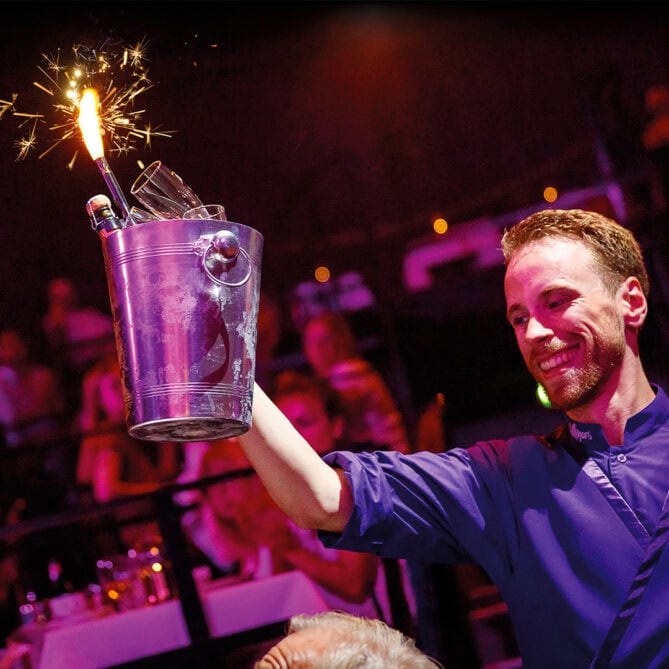 Male waiter smiling and serving a bucket of champagne with fireworks.