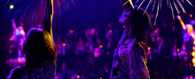 To artister med armen i vejret og glimtende tøj og fyrværkeri i baggrunden i Cirkussalen.